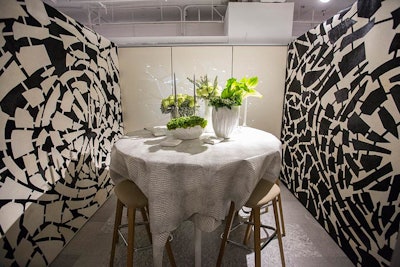 Gensler designed a booth for Teknion/Studio TK. The installation had imagery inspired by broken mirrors, with custom wall coverings on either side and projections of glass shards along the back wall. The round table had white, textured linens, and bright green floral arrangements.