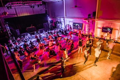 During a warm-up session, sections of the Folsom Street Foundry were bathed in purple, red, and yellow lighting. Each section had a separate instructor and exercises.