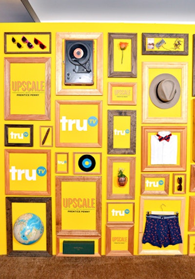 A bold yellow press wall included framed logos and objects evocative of an upscale lifestyle—such as a fedora, a bow tie, sunglasses, and a globe.