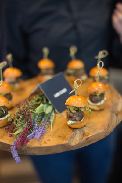 Lamb sliders were presented on a rustic wooden platter decorated with fresh herbs and flowers.