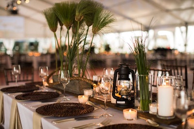 Tabletop decor included decorative turned rope, custom wood plinths, papyrus grass, and classic camping lanterns. Above diners, a starlight pattern appeared on the ceiling of the tent.