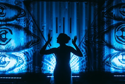 An attendee appeared in silhouette in front a shipping container onto which the III Points logo—an upside-down triangle—was painted alongside a mural bathed in blue light. The logo represented the three points of the festival: music, art, and technology. Shipping containers were used during the event as decor, and doubled as trailers.