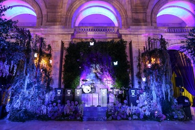 To create a dark woodlands fantasy theme, Emily Clarke Events designed a setup that included a variety of florals and greenery illuminated with purple and blue lighting. Animated butterflies surrounding the Astor Hall stage added to the event aesthetic.