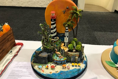 Condensed milk and coconut flour created the sand on the base of this novelty cake for the “Under the Florida Sun” theme. Strands of spaghetti were used to support the umbrellas, rollercoaster, and some animals.