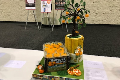In this creation, the plaque on the front of the crate was handpainted with cocoa butter. Stenciling and airbrushing created the honeycomb designs on the cake that serves as the base of the tree, which has leaves and oranges made of modeling chocolate and fondant. Oranges and blossoms on the board are blown sugar.