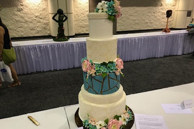 The cream-colored layers of this wedding cake were painted with ivory pearl dust and steamed to look like satin, and to allow the edible lace to adhere. The turquoise layer was painted bronze, then covered in shapes painted with cornstarch and gel food coloring, and scratched with a wire brush to make that portion of the cake look distressed.