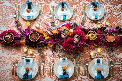 Looking to provide Diwali-theme ideas, Nuage Designs enlisted Tinsel Experiential Design to design a tablescape in keeping with the holiday. Orange Hemp Flocking linen reminiscent of traditional henna designs was provided by Nuage for the base of the design. A floral runner in bright fuchsia, yellow, red, and orange was strung across the table in keeping with the colorful nature of Indian celebrations. Party Rental Limited's gold florentine plates were topped by Nuage napkins to complete the festive table.