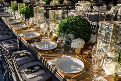 The long dinner tables that anchored the room were made of reclaimed wood, adding a further element of texture to the dining room. Accented by rows of mercury glass hurricanes and large preserved boxwood spheres that offered pops of color, together they created visual interest without disrupting guests' line of sight.