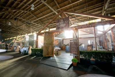 Hensley Event Resources created a lodge-like structure for its vignette. String lights added warmth to the space, which was filled with rustic wooden furniture and blue-and-gold tablecloths, as well as simple florals by Scarlett & Grace and food by Checkers Catering and Special Events. The lodge was surrounded by green hedges.