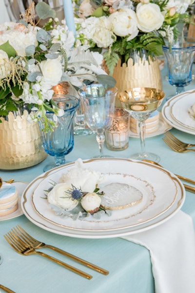 The Festive Frog used a mix of vintage and new china for the place settings. Contemporary gold flatware and vintage gold-rimmed glassware provided an elegant yet neutral palette to offset the bright blue linens from BBJ Linen.