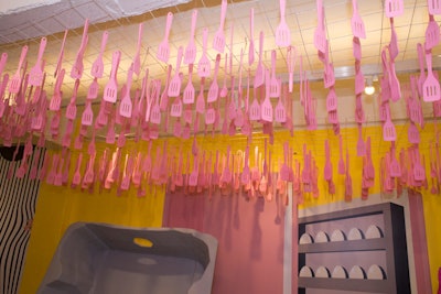 Hanging above the egg carton is a ceiling installation created with pink spatulas and whisks, familiar tools to anyone who cooks with eggs.