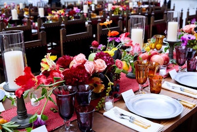 Caravaggio-inspired centerpieces contained fruit—such as apples, pears, pomegranates, figs, and grapes—and flowers—including poppies, roses, cascading ivy, and banana grapes—with hurricane candles in the middle. The tables were set with pewter charger plates and off-white china, along with pearl-handled flatware with antique silver details, linen napkins, and blown glass goblets in amber and plum.