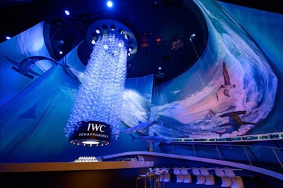 At luxury watchmaking convention Salon International de la Haute Horlogerie, held in Geneva, Switzerland in 2014, IWC Schaffhausen chose a water theme. Aiming to celebrate its Aquatimer collection, the trade show booth was meant to evoke the feeling of diving into a wave. Replica hammerhead sharks hung from the ceiling, surrounding a central chandelier comprising 2,400 individually strung Plexi 'bubbles' that hung nearly 30 feet down. Two cross projectors cast deep sea images both vertically and horizontally onto two large curved screens, while a circular bar in the middle of the space housed an information desk and a bar that served cocktails and even caviar.