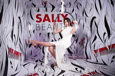 Retailer Sally Beauty had a carnival-theme booth complete with acrobat performers, games, and a miniature Ferris wheel of products. A branded photo backdrop featured illustrated black and white hair with red combs; guests sat in a spinning hoop to get their photos taken. The activation was designed and built by Conversate Collective.