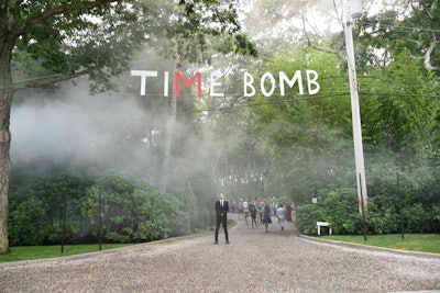 The Watermill Center's 25th-anniversary benefit, titled 'Time Bomb,' welcomed over 1,000 guests. This year's entrance was unmistakable with a large cloud of hazy smoke greeting those arriving on Water Mill Town Road.