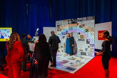 A photo booth in the Wells Fargo 'Equality' lounge showcased the company's sponsorship of an exhibit at the Newseum opening in March 2019, called 'Rise Up: Stonewall and the LGBTQ Rights Movement—50th Anniversary (1969-2019).' The photo booth featured a backdrop of newsprint with headlines from the time period, accented by a neon rainbow.