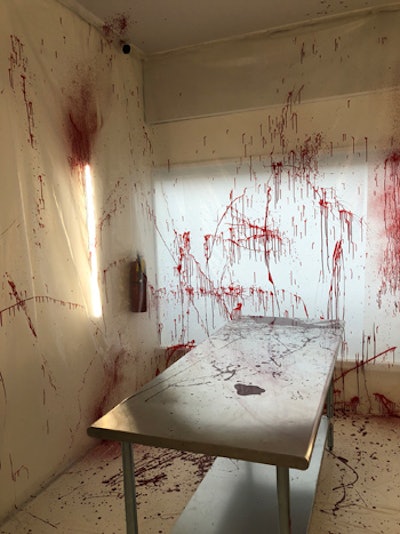 A blood-splattered autopsy room includes plastic sheeting and a metal table.