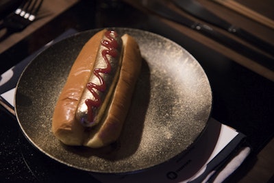 Food and beverage from Love Catering also reflected life as a young adult—with an elevated twist. Featuring items that young roommates might find in their shared kitchen, fun dishes included gold-covered hot dogs with bacon (pictured), tie-dye spaghetti alfredo, and chocolate sprinkle doughnuts with bacon, tomato, and ketchup.