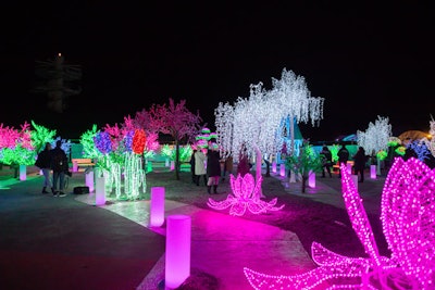 A winding path showcases trees dripping with icicle lights and blooming neon flowers