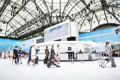 For his Spring 2016 show in October 2015, Lagerfeld transformed Paris’ Grand Palais into his very own Chanel airport. A pristine Chanel Airlines terminal greeted guests upon arrival, complete with a faux airport exterior, and the departures board heralded flights to the cities of Chanel events: Shanghai, Dubai, Salzburg, New York, London, and Rome. Not only was Chanel luggage shown on the runway, but so were cheeky sporty sandals with embedded LED bulbs that mimicked airplane floor lights.