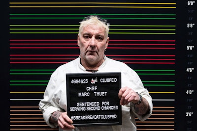 Chef Marc Thuet, who curated the menu's sandwiches and sides, posed in front of a colorful mugshot photo wall with an open-face letter board.