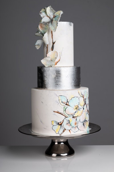Another Dbakers cake is the Silver Flower: dark chocolate cake filled with passion fruit curd and covered in white fondant. Decor includes watercolor flowers with silver leaf accents and 3-D hand-painted wafer paper flowers.