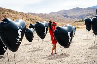 YSL Beauty's first Coachella activation, designed and produced by AKJOHNSTON Group, resembled a gas station with vintage convertibles, a massive lipstick sign, and hot pink gas pumps. Next to it was a field of black balloons with the YSL Beauty logo, creating a unique photo op in the desert environment.