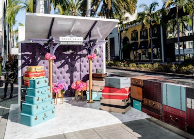 Rodeo Drive's latest social art installation, designed and produced by AGENC, is inspired by the 'jet setter' lifestyle that many of the iconic street's shoppers have or aspire to. The photo-friendly vignette has sets of luxury luggage and colorful flowers; on the back side, an additional photo op has a wall of stylized passport stamps.