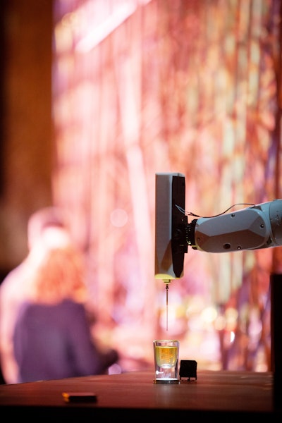 The 3-D printer’s robotic arm dips a long needle into the glass, injecting droplets into the drink.