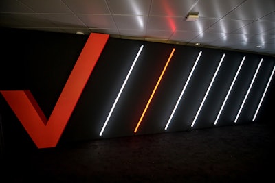 Sleek, minimalist decor elements included Verizon's red logo on a wall, followed by neon light fixtures placed diagonally.