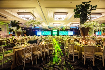 In the dining room, HMR Designs strung large willow chandeliers, foliages, and fairy lights from the ceiling. On the tables, they topped risers with large fiddle fig trees.