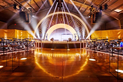 For the debut Sound by SoulCycle event in Los Angeles, “the creative concept for the concert centered around ‘sound as sanctuary.’ Guests entered the hangar-esque, nightclub-like space through a wheel-like portal, reducing the guest experience to a meditative tunnel where affirmations were delivered via sound-isolation pods…. At the center was a studio-stage hybrid, stylized like a bent-wheel where enthusiasts powered the light stage with their energy.”