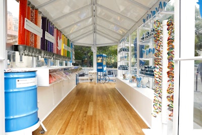 The candy shop was housed in a greenhouse-style trailer. Candy arranged by color served as a background for printed-out tweets. Additional treats included custom fortune cookies, rainbow lollipops, rock candy, and gummies. The trailer also offered popcorn in a blue antique-style popcorn maker.