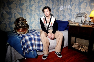 On December 11, Spotify hosted a listening party for Harry Styles's new album, Fine Line. The private fan event aimed to evoke the fictional seaside land of 'Eroda,' a reference from the singer's new song 'Adore You.' Held at a private home in Los Angeles, the gathering transported guests to Eroda with lush scenery, fishermen serving sashimi, boats docked on a small lake, staffers wearing branded raincoats, and a vignette called 'Harry's Little Blue Bedroom' (pictured). Styles himself made a surprise appearance at the event to hand out tickets to his December 13 show at the Forum, and fans were able to hear the new album in full.