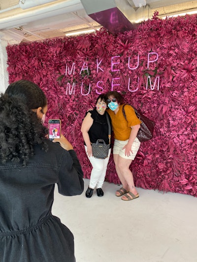 Guests pose for a photo in front of a floral wall while wearing masks at the recently opened Makeup Museum.