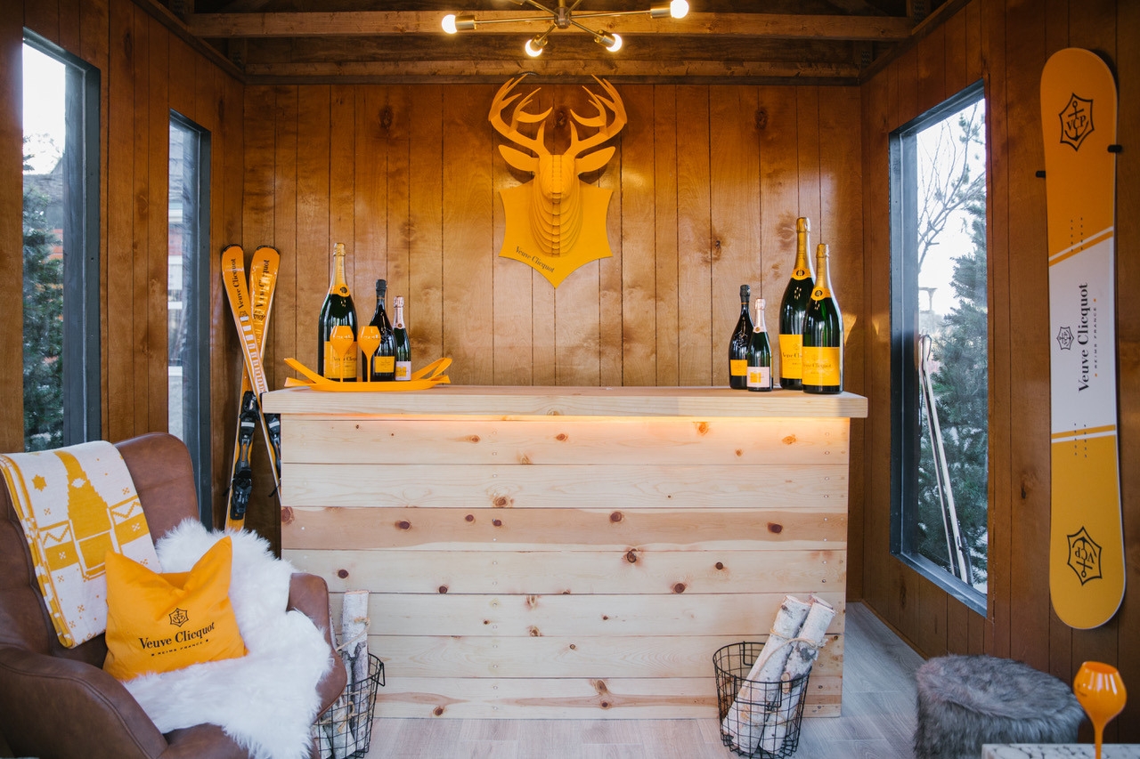 The chalet draws inspiration from European design elements, woodsy cabins and the luxury of the Veuve Clicquot brand—all of which is seen in the space's leather seating, faux- fur throw blankets, and custom wooden bar and light fixture.