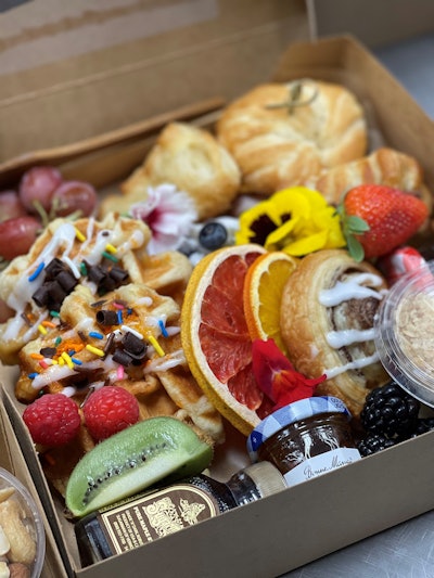 Brunch box with house-made waffles, house-made croissants with bourbon butter and Georgia syrups, house-made granola mini parfaits, berries, grapes and edible flower garnish, from Proof of the Pudding in Atlanta