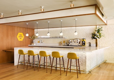 While the space is not overtly branded, it does feature nods to Bumble’s iconic honeycomb motif with subtle hexagonal shapes in the bar tile and ottomans. Vintage danish opaline glass pendants hang over the bar.