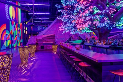 Venues are a great place to find design and color scheme inspiration too. Located inside AREA15 in Las Vegas is Oddwood, a colorful cocktail lounge from Corner Bar Management. The highlight of the 2,500-square-foot venue is a 23-foot-tall digital maple tree made from 5,000 individually programmed LED leaves, all of which change colors depending on the beat of the music. The rest of the venue is filled with large-scale murals, plus a mix of brass, bronze, and wood bar tops and surfaces. The psychedelic space can hold 122 people.