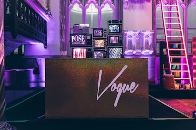 In June of 2018, FX’s then-newest series Pose celebrated its release with an over-the-top event at Harlem Parish—a former church-turned-cultural center. Pose’s event nodded to the series as a tribute to the queer ballroom world of New York in the 1980s in a number of ways—from one bar decked out in gold mannequin heads wearing brightly colored wigs to another neon library-themed bar, a makeup vanity station and, of course, the DJ booth. Paying homage to voguing, a dance that originated in the queer ball community, the sparkling black booth boasted “Vogue” in large purple lettering and was backed by vintage TV props displaying the show’s name. See more: Strike a Pose: How FX Threw an Authentic 1980s Queer Ball