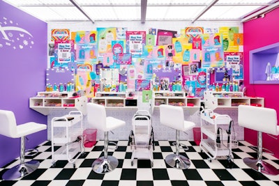 Inside, on-site professional stylists were giving attendees hair styles reminiscent of the ‘90s and early 2000s (think: crimping and butterfly clips). The salon itself was bursting with color and design, from a black-and-white-checkered floor to a collage-style mural featuring OGX’s products, an “XOXO” wallpaper design, and more.