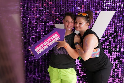 Guests pose for a photo against a branded, purple sequin wall.