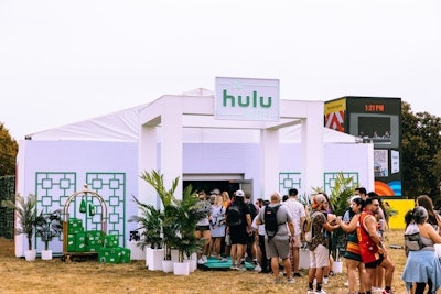 The Hulu Motel concept also popped up at Austin City Limits earlier this month. The activation, produced by Live Nation, was an enclosed space with air-conditioning, seating, and drinks set up in a retro-style enclosure with faux wood paneling and concert-style posters. In keeping with the motel theme, the outside area featured a luggage cart setup with green suitcases and branded stickers. The Hulu activation also included international-mailable postcards featuring artwork from the facade of the space. People were encouraged to write their own postcards and mail them directly from the activation.