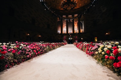 Lush arrangements of white, pink, and red roses by Lewis Miller Design lined the runway, playing off the pink jacquard suits and gowns in the collection. Siriano’s message about the collection in the show notes said: “Welcome to Audrey Hepburn’s rose garden at midnight.”