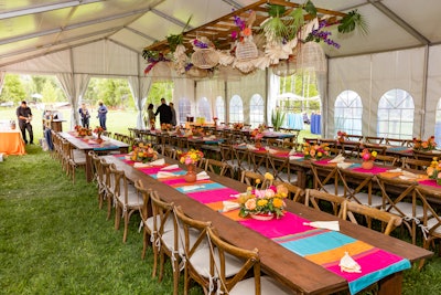 Beth Gill and her team from Aspen Branch were at the helm of the decor. Inside the tent was a massive centerpiece over the farm-style tables, which were accented with handwoven baskets; palm fronds; a garland of corn husks; and vibrant orange, pink, and purple tropical flowers. Tables were topped with matching runners that included additional corn husk garland, citrus-hued ceramic vases, and an array of fresh florals.