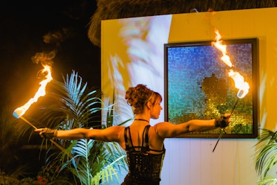 A fire dancer performs in front of an inverted disc wall depicting the coastal tides of the Maldives.