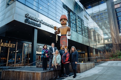 Celebration of Art speakers and dignitaries pose in front of 'Mowitch Man' by Andrea Wilbur-Sigo at the entrance to the Seattle Convention Center's Summit building.