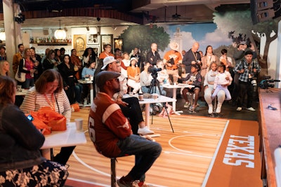 The entrance hallway featured neon lights on the ceiling as well as a chair area where guests could get custom laces added to their shoes. The interior leaned into the college aesthetic, with the school’s official burnt orange and white colors everywhere, the floor mimicking a basketball court, a large photo mural of the campus, and the hallways leading to the bathrooms decked out to look like locker rooms.