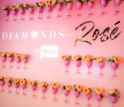 The event step-and-repeat features hot pink wine glasses filled with orange florals.