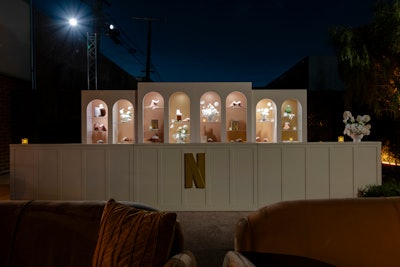 Upon entry, this bone white and gold shelving housed the 'shoe valet,' where guests could trade high heels for branded sherpa slippers. The slippers were displayed in warm white lighting alongside monochromatic books as props.